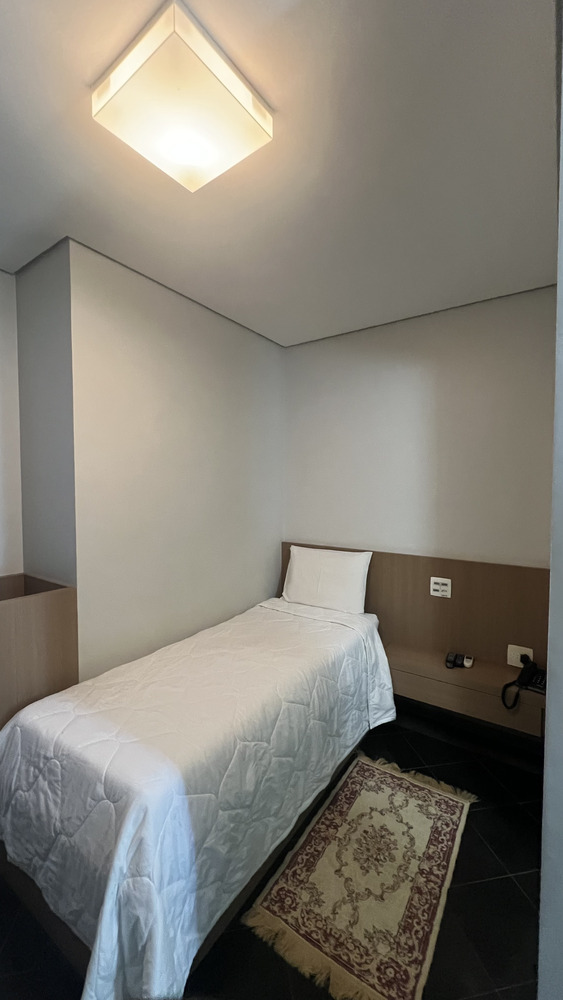 Quarto compacto do Residence Hotel com cama de solteiro, ar-condicionado e banheiro privativo